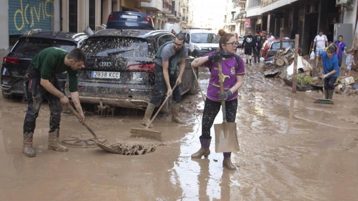 Trabajos de limpieza en las calles de Algemesí tras la inundación con dos personas arrastrando agua y barro hacia el alcantarillado.