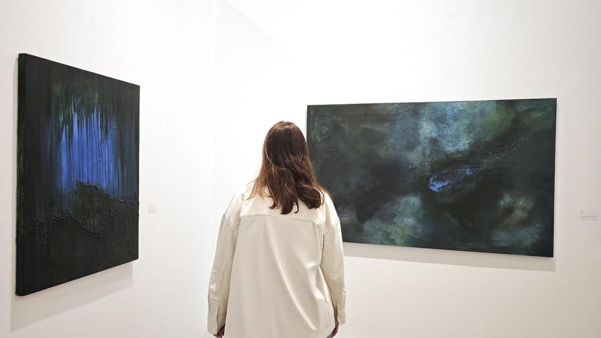 Una espectadora contempla los cuadros de Paz Banciella en la sala de exposiciones de la Universidad de Oviedo.