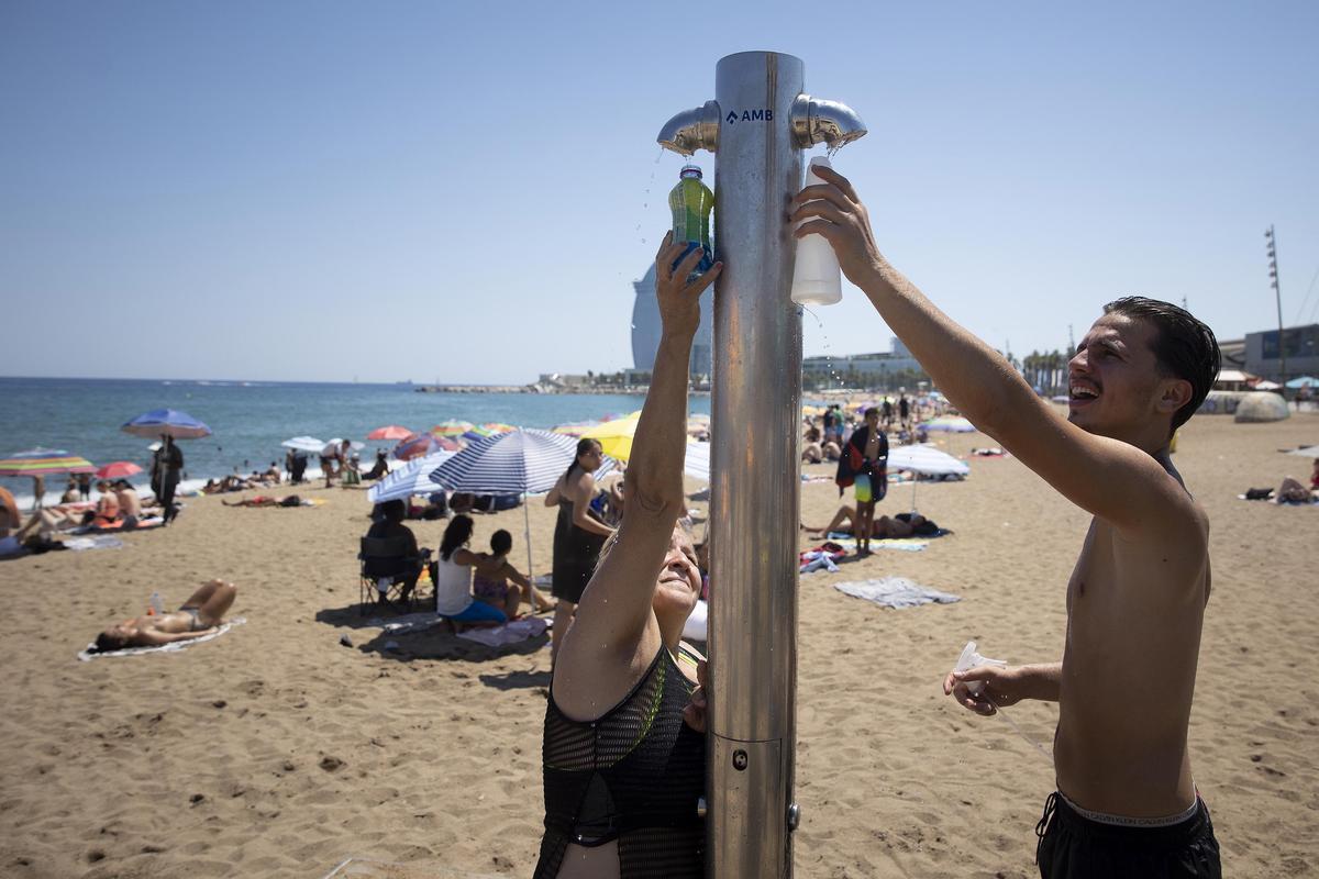 Dos bañistas en las duchas públicas de la playa de Sant Sebastià de la Barceloneta, hoy