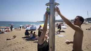 Dos bañistas en las duchas públicas de la playa de Sant Sebastià de la Barceloneta, hoy