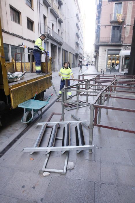 Carrers amb restes de mobiliari urbà cremat, contenidors per terra i treballadors de la brigada treballant