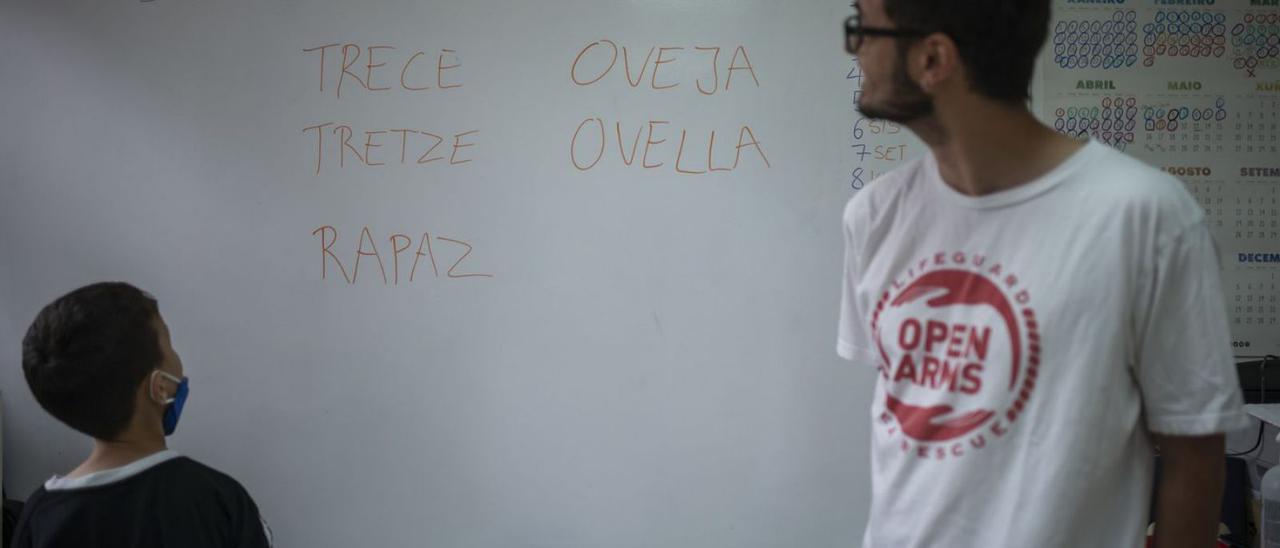 Un escolar en la pizarra con algunas palabras en gallego y catalán, ante la mirada de Ferrán.   | // B. LORENZO