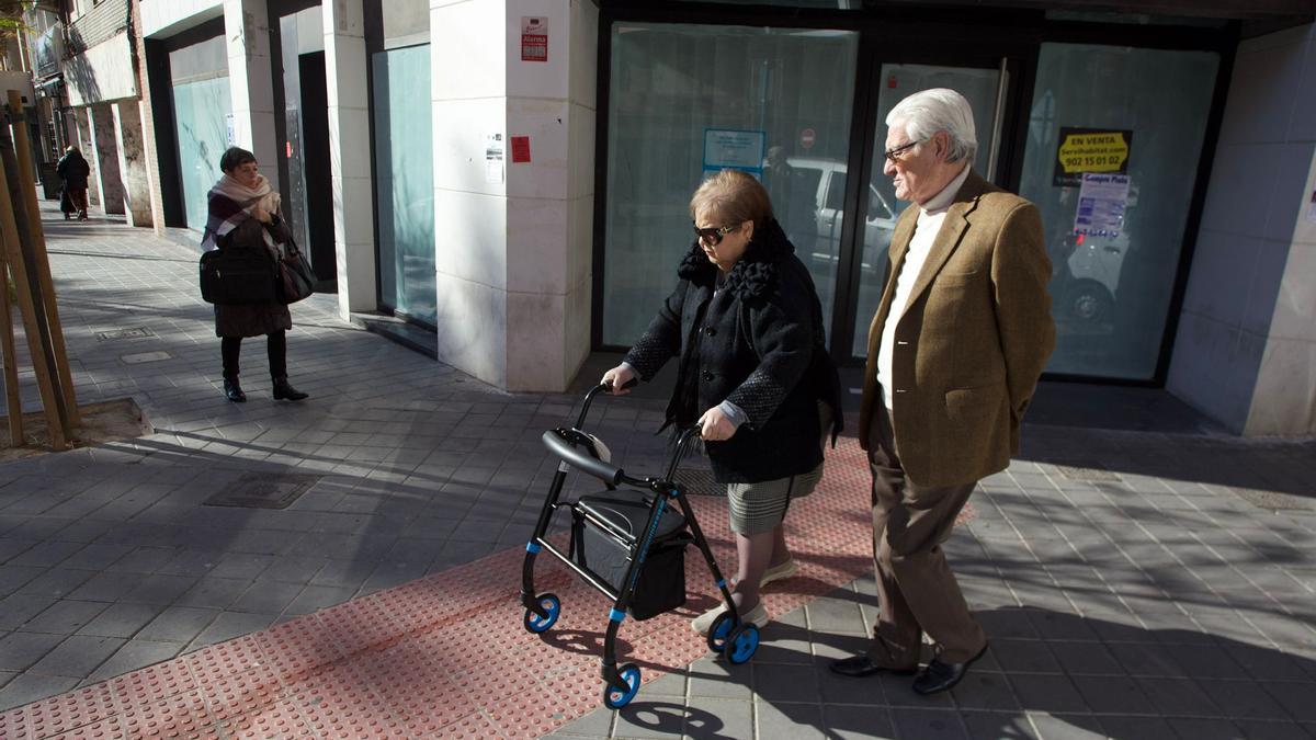 Dos personas mayores pasean junto a una sucursal bancaria recientemente cerrada en Benalúa.