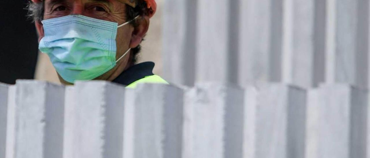 Un trabajador con casco y mascarilla, en una obra.