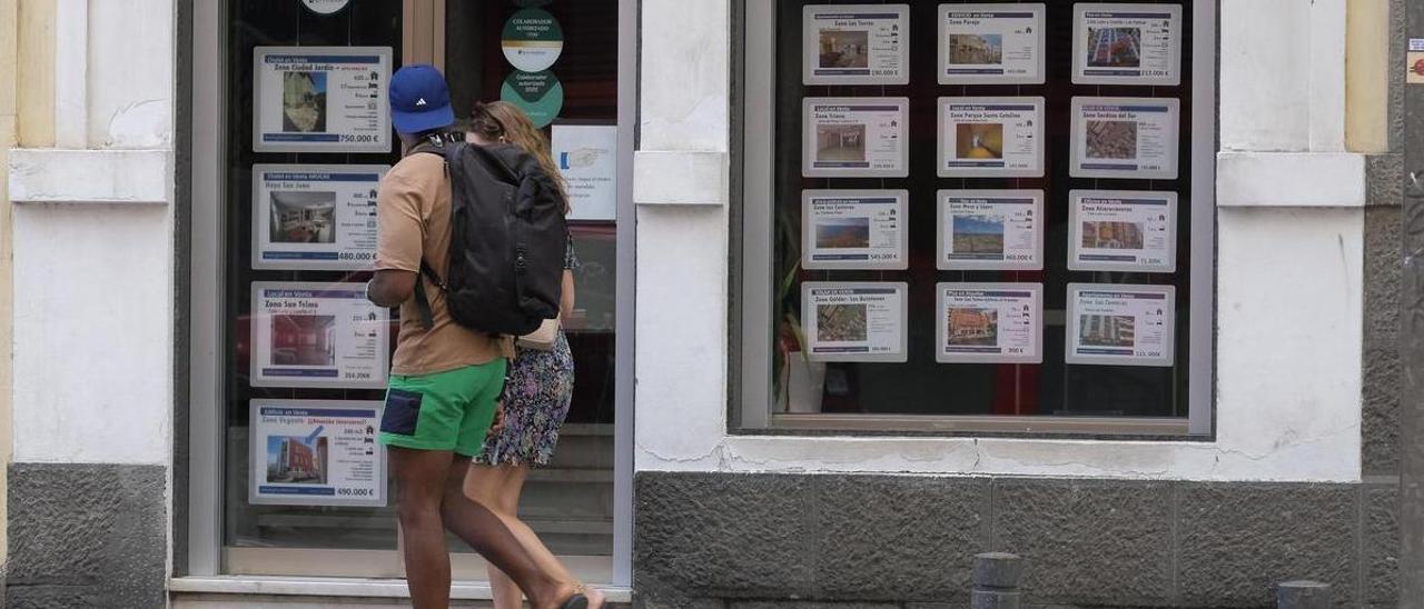 Dos ciudadanos pasean junto a una oficina inmobiliaria.