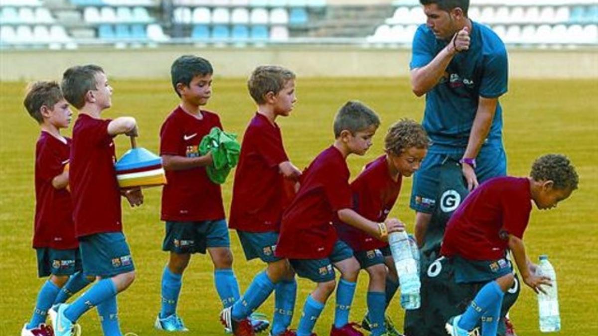 Unos niños atienden las instrucciones de un monitor en una de las concentraciones de fútbol base del Barcelona de este verano.