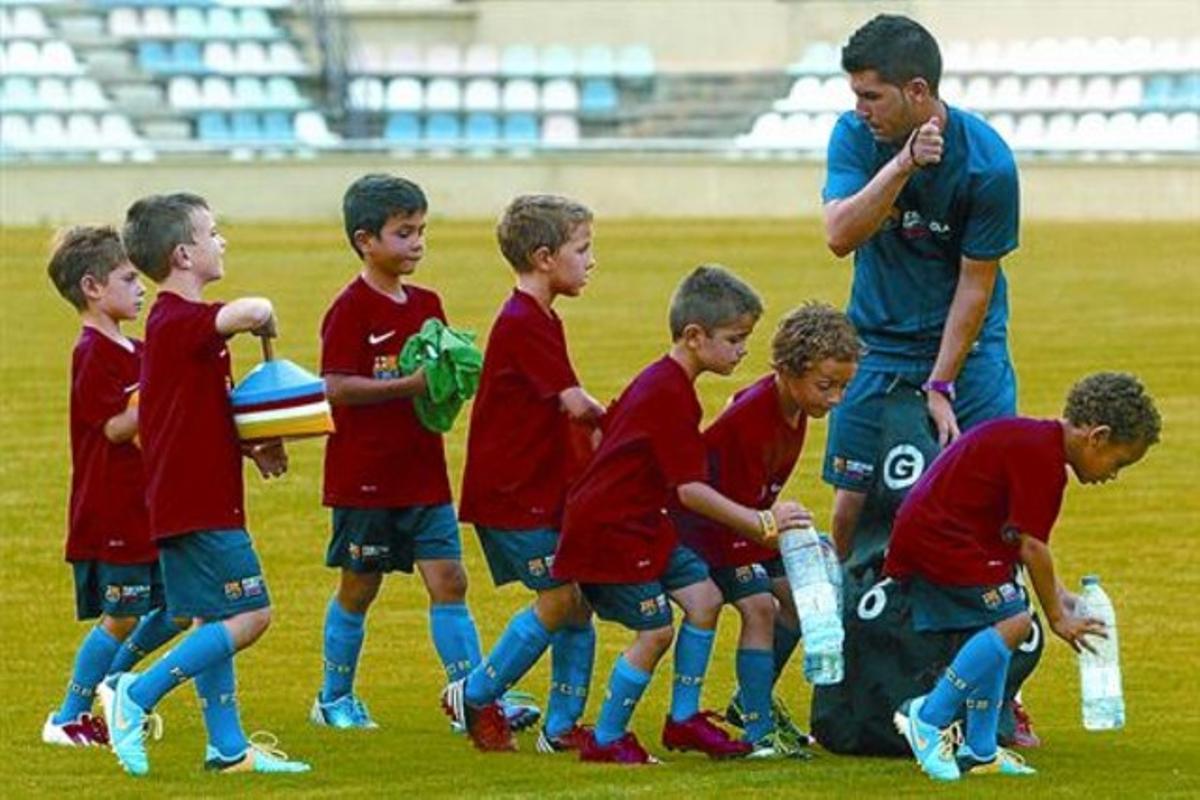 Unos niños atienden las instrucciones de un monitor en una de las concentraciones de fútbol base del Barcelona de este verano.