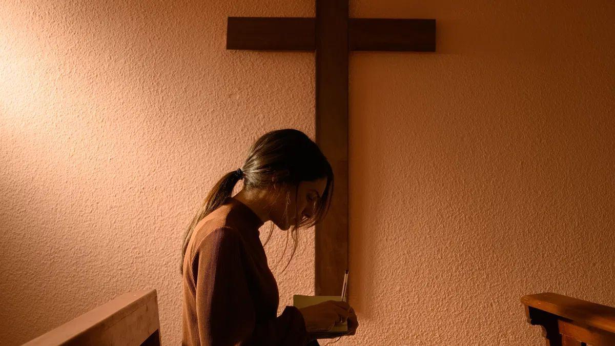 Una joven reza ante un crucifijo.