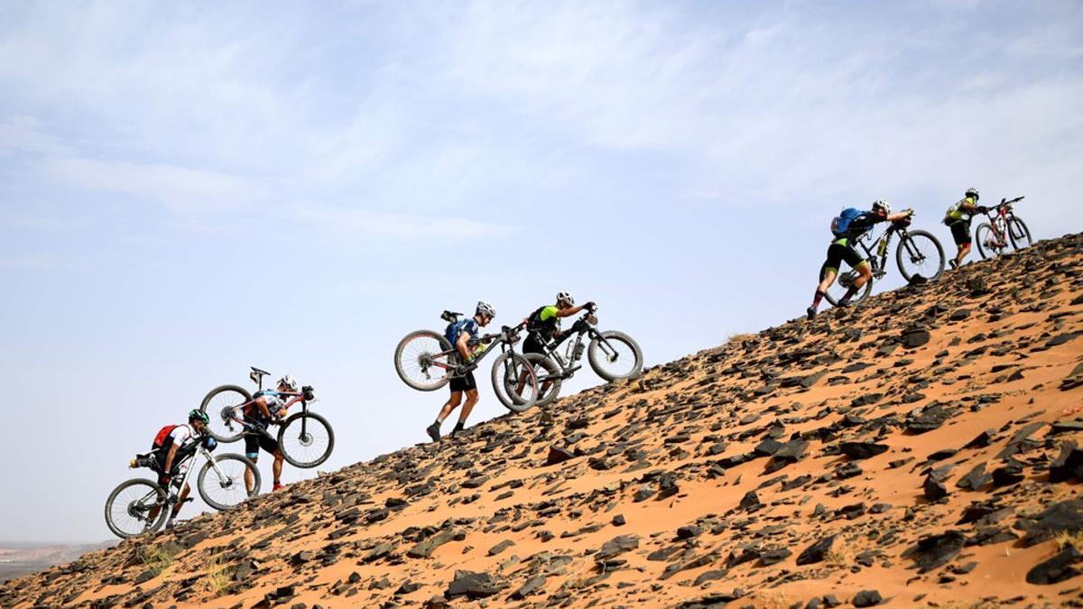 Los competidores llevan sus bicicletas a lo largo de una duna de arena durante la Etapa 2 de la 14ª edición de la carrera de ciclismo de montaña Titan Desert 2019 entre Merzouga y Ouzina.