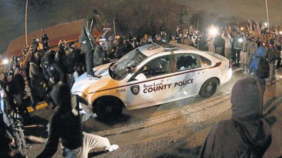 Altercados 8 Una muchedumbre asalta un coche policial en Ferguson, en la madrugada del lunes.