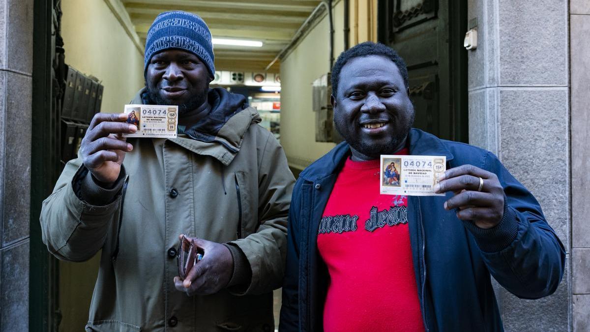 Dos ciudadados gambianos residentes en la población de Olot, posan frente la administración de lotería número 1 de Olot (Girona).