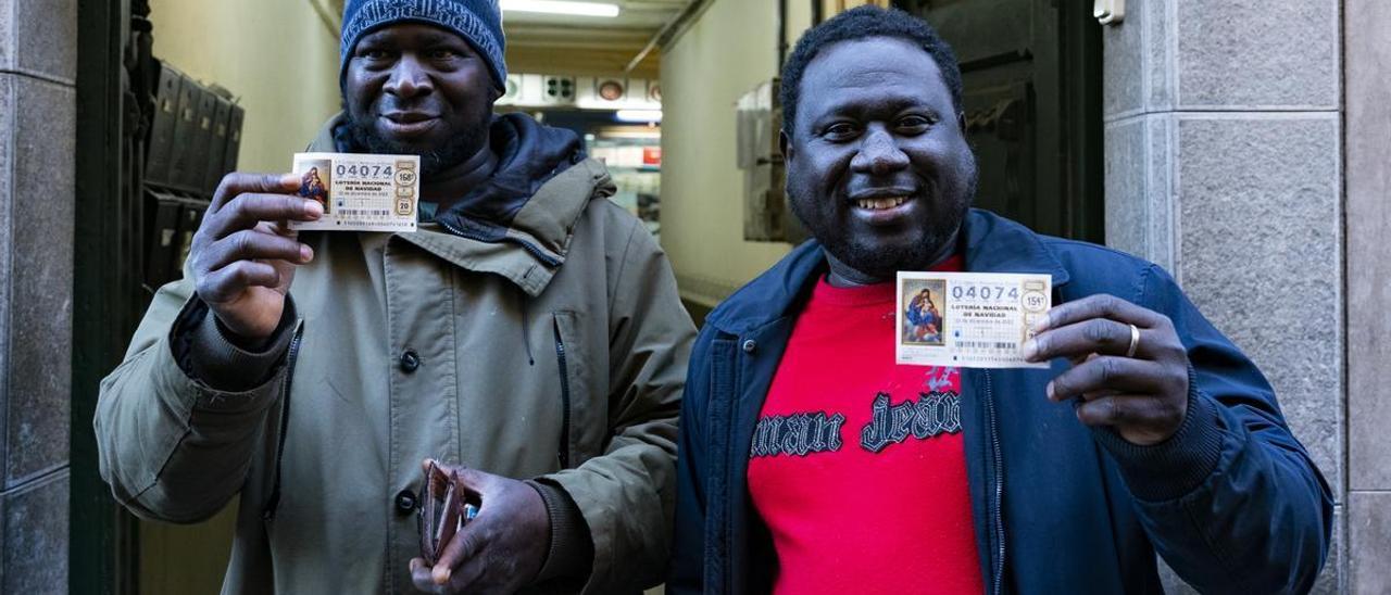 Dos ciudadados gambianos residentes en la población de Olot, posan frente la administración de lotería número 1 de Olot (Girona).