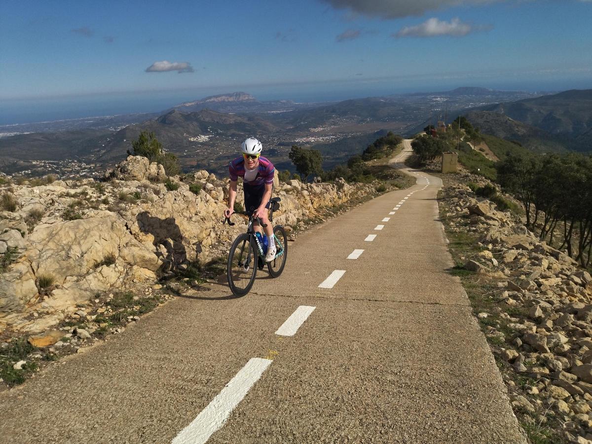 Los corredores profesionales se retuercen sobre la bicicleta. A lo lejos, se divisan el Montgó y el mar