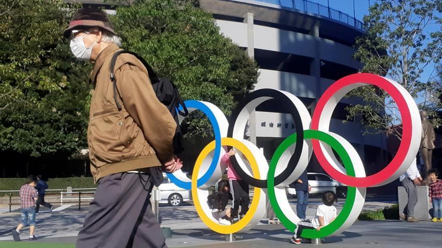 Un hombre con mascarilla junto al logo de los JJOO en Tokio.