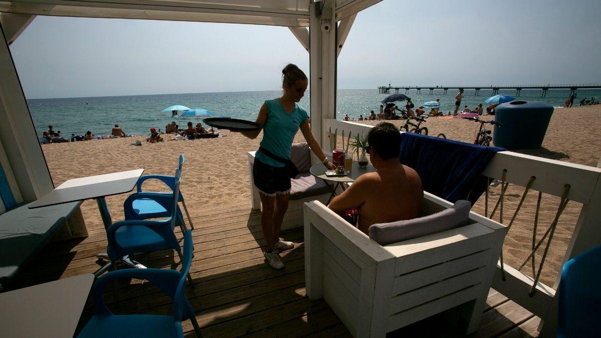 Una camarera sirve una consumición a un cliente en un chiringuito de playa en Barcelona. /