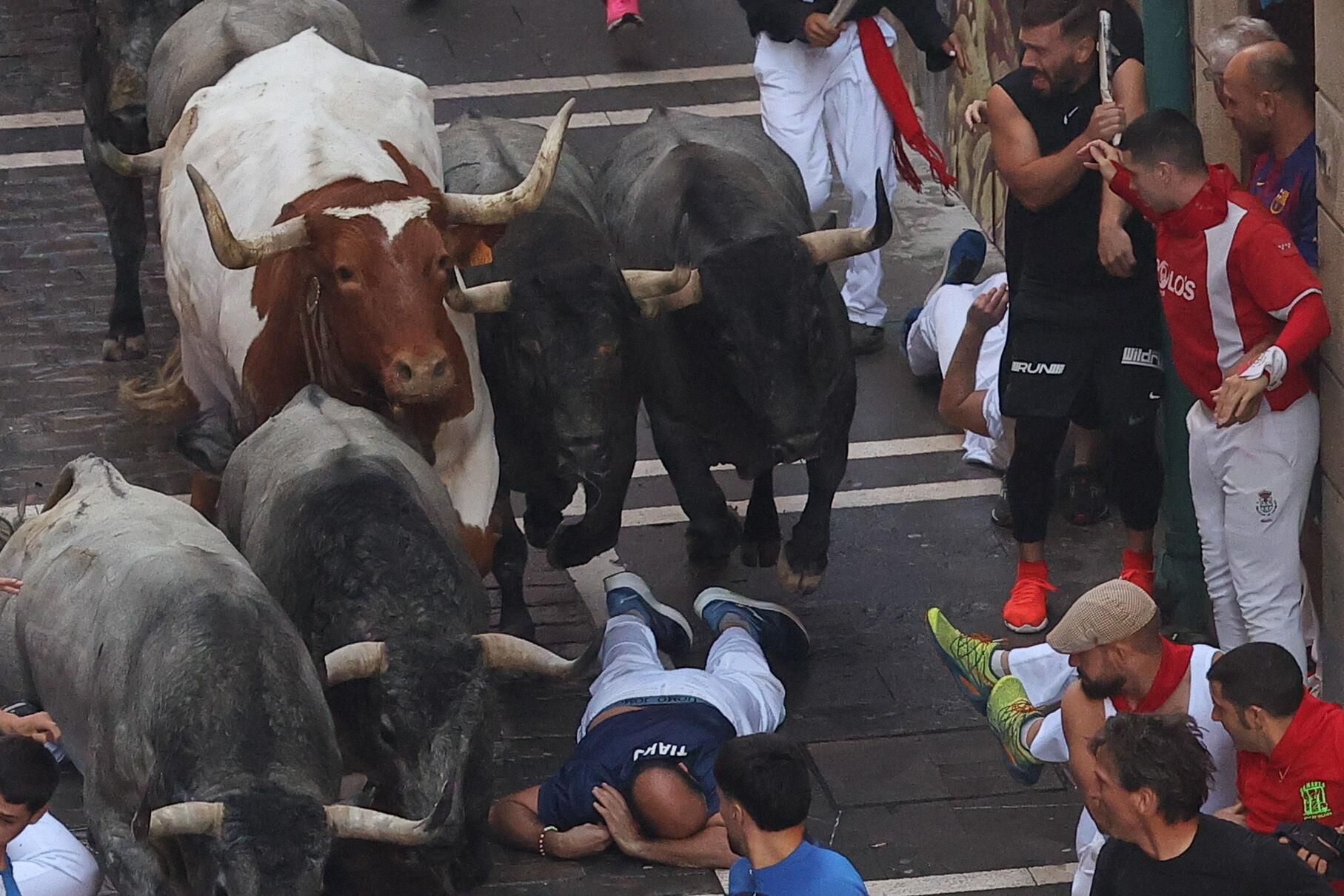PAMPLONA, 12/07/2025.- Un mozo cae al paso de los toros de la ganadería de José Escolar en el tramo inicial de la Calle Estafeta desde la curva de Mercadere,s, en el sexto encierro de los Sanfermines, este sábado en Pamplona. EFE/J.P. Urdiroz