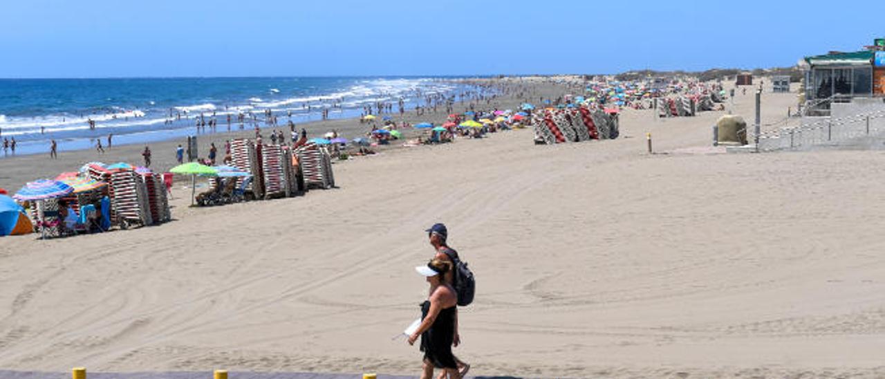 Dos turistas caminan por la pasarela de madera de Playa del Inglés, en el sur de la Isla .