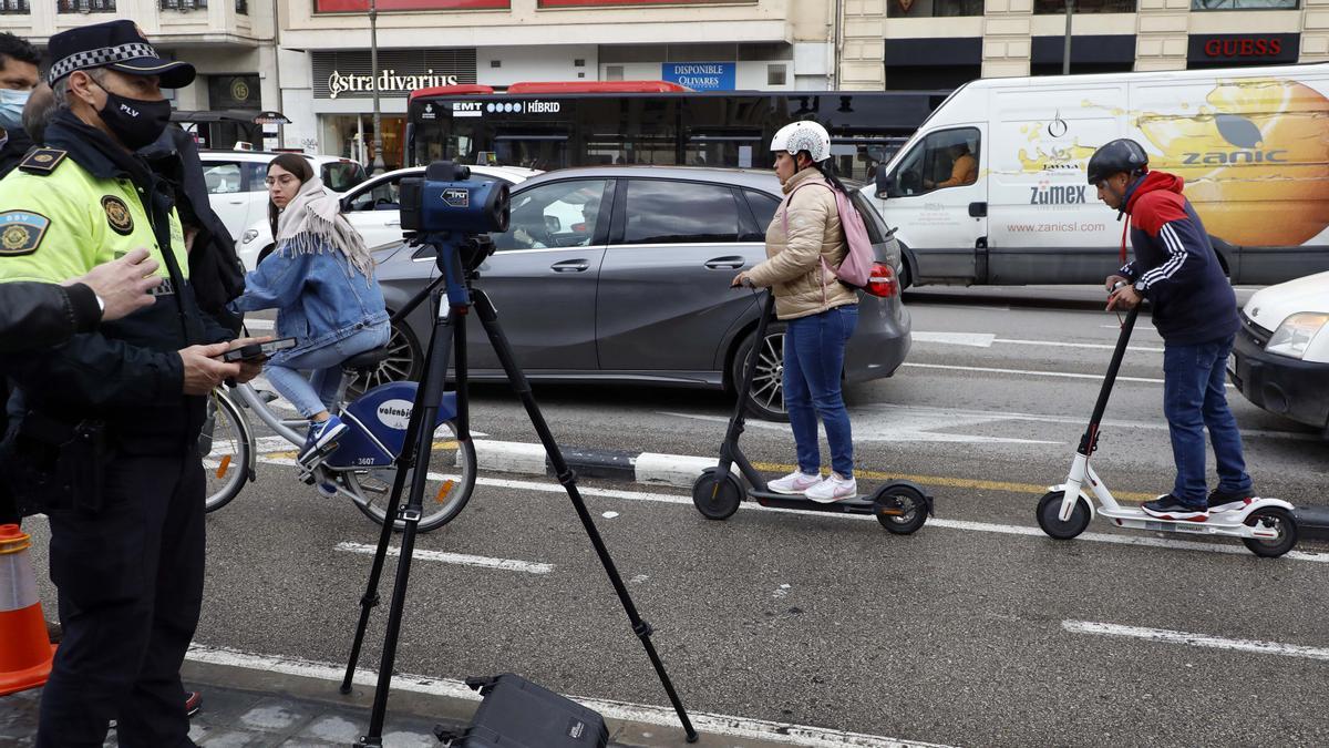 Un agente controla la velocidad con una tablet y el radar, mientras dos conductores circulan en patinete por la calle Xàtiva.
