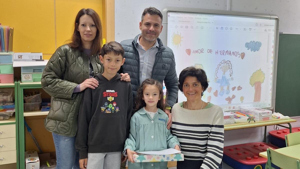 La pequeña Marta González, con sus padres María Álvarez y Daniel González, su hermano Mario y María Milans, profesora de religión del colegio de La Fresneda, el día de la entrega del premio con el trabajo ganador en la pizarra digital.