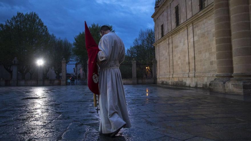 Un cofrade del Silencio tras la suspensión de la procesión por lluvia en 2019.  Arriba, la Soledad cubierta con un plástico, urna de metacrilato de Jesús Yacente y el público con paraguas a la salida de la Tercera Caída.