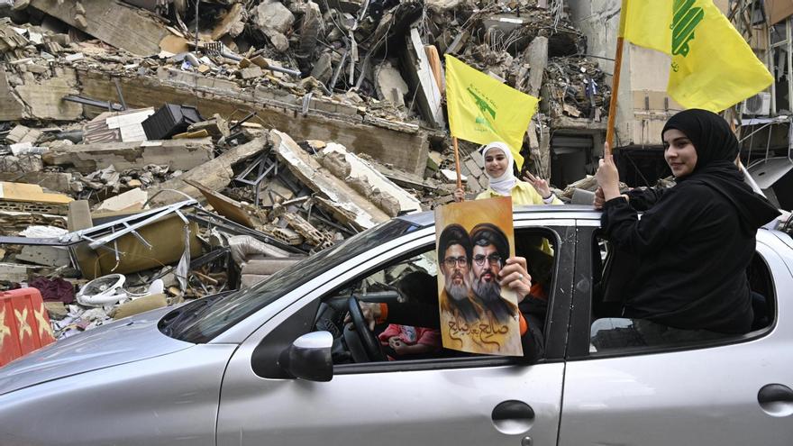 Dos chicas ondean banderas de Hizbulá y otra persona muestra una foto de Hasán Nasrala en una calle de Beirut, celebrando el alto el fuego.