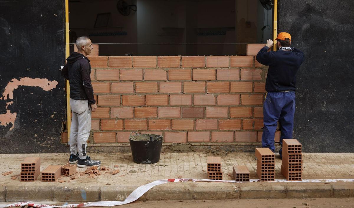 Dos trabajadores levantan un muro en la entrada de un club deportivo de Paiporta, el pasado 18 de noviembre. | EFE/BIEL ALIÑO