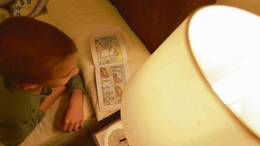 Un niño lee en su cámara a la luz de una lámpara.