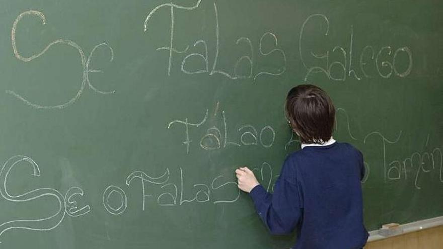 Un alumno escribe en gallego en la pizarra de un aula.