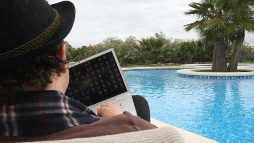Un hombre trabaja con su ordenador junto a una piscina en una urbanización de Alicante.