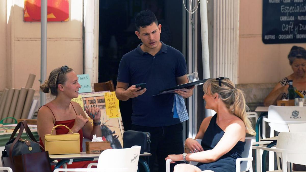Un camarero atiende a unas clientas en un establecimiento de hostelería de Málaga. | ÁLEX ZEA