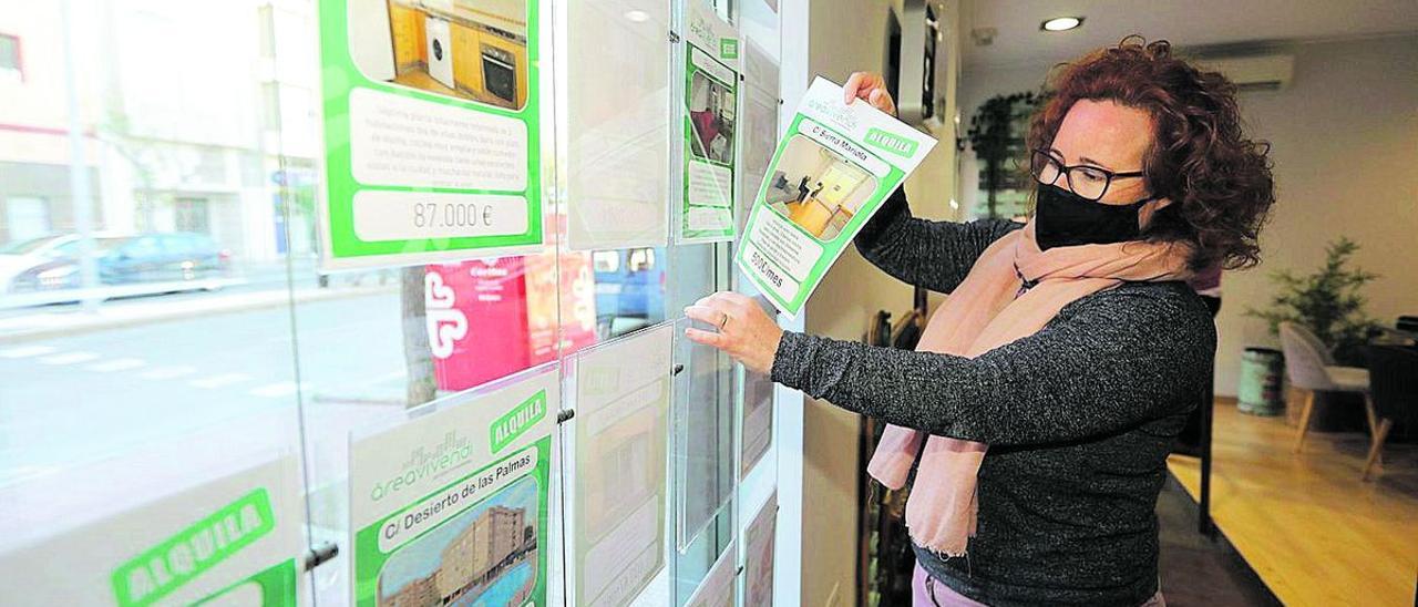 Una agente de la propiedad inmobiliaria coloca unos carteles en el escaparate de una agencia de Castelló.