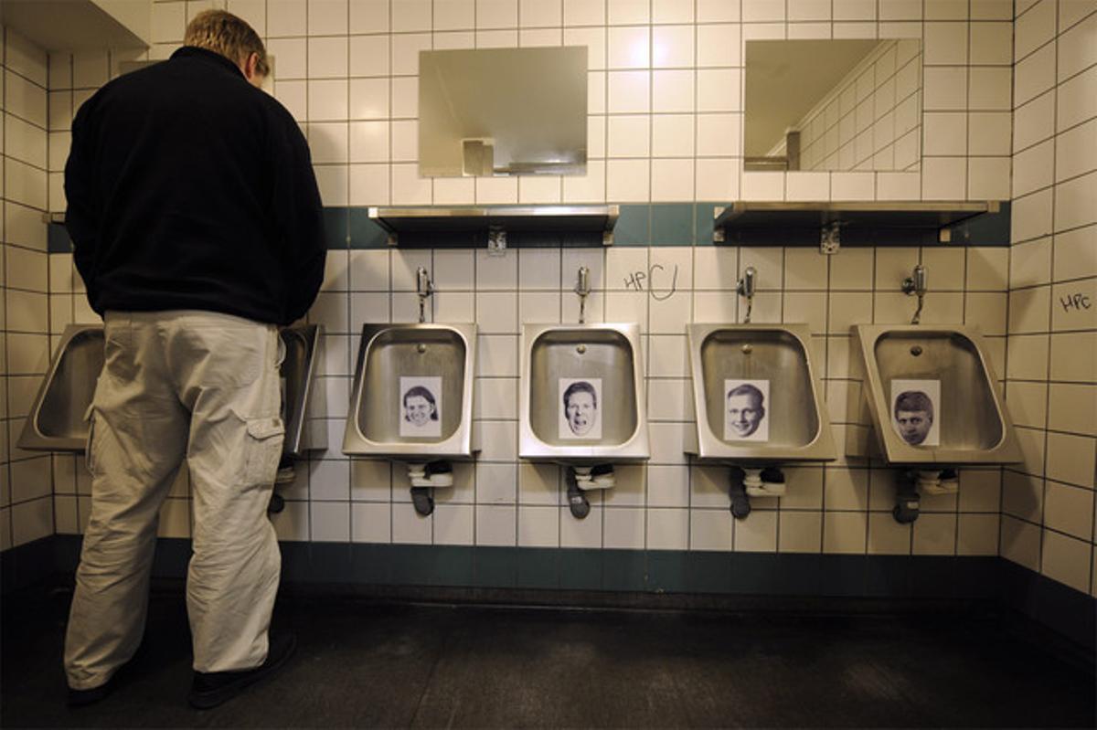 Un hombre orina en el lavabo de un bar de la capital con fotos de banqueros que huyeron del país.