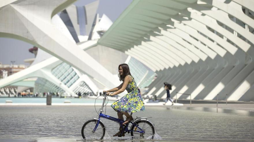 Una joven pasea con su bicicleta por una de las láminas de agua de la Ciudad de las Artes y las Ciencias de Valencia.