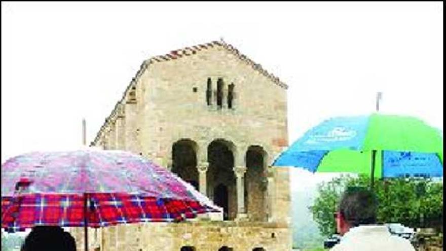 Dos turistas, ayer, con paraguas, delante de Santa María del Naranco.