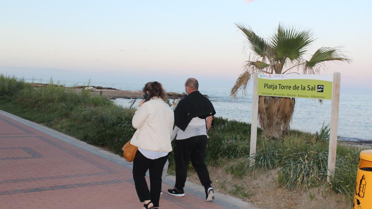 Dos viandantes caminan por el paseo marítimo de Torre la Sal.