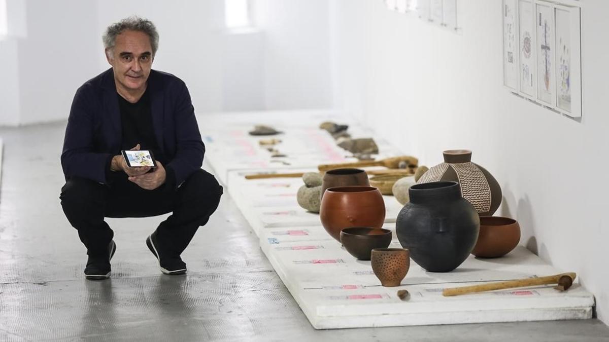 Ferran Adrià sostiene un móvil con la 'app' Tu cuento en la cocina junto a objetos de cocina del Neolítico, en el BulliLab.