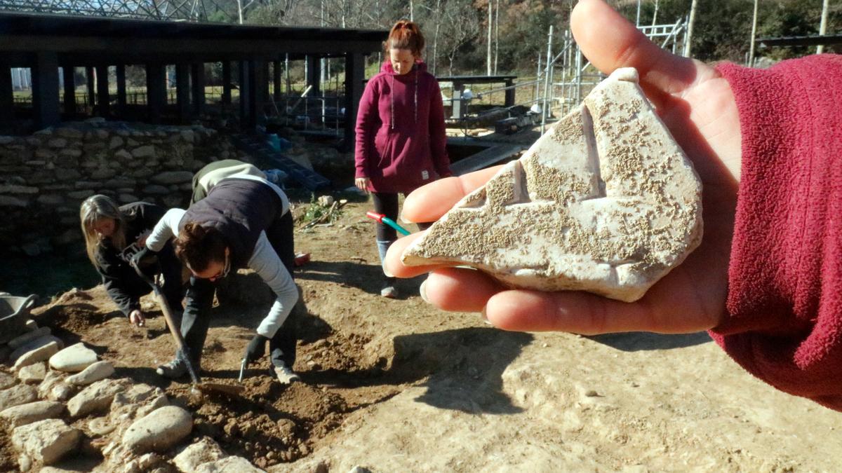 En primer terme, el fragment d'inscripció; al fons, els arqueòlegs excavant el pati de la vil·la romana del Pla de l'Horta