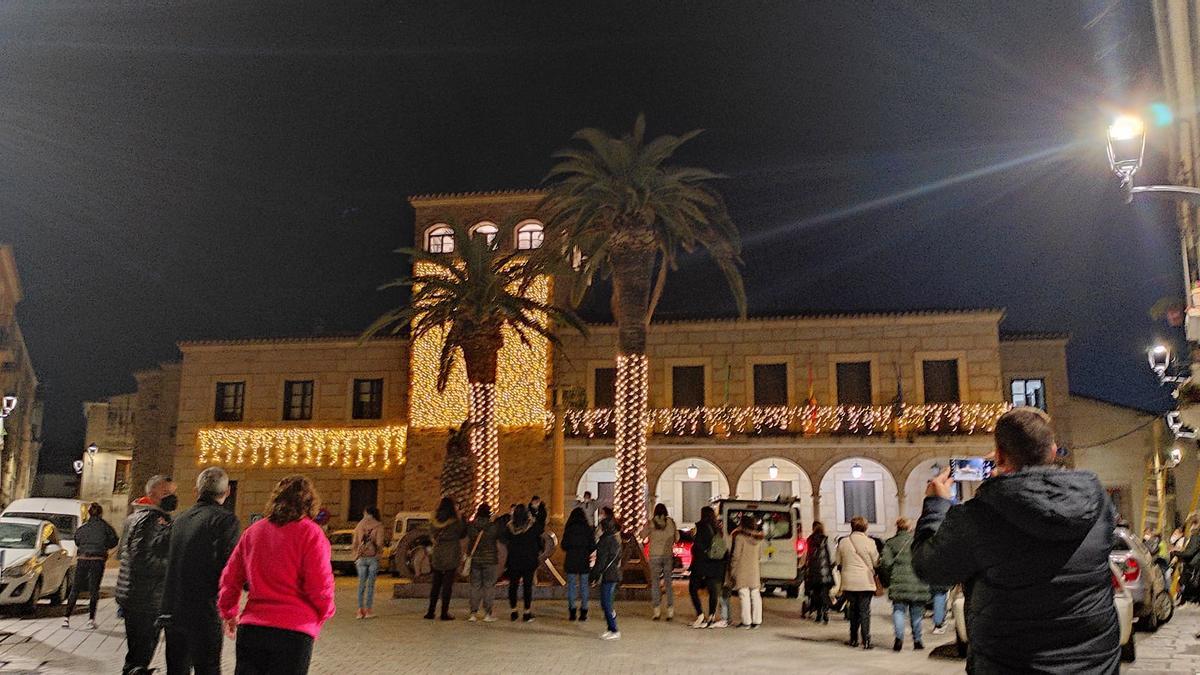 Varias personas observan la iluminación navideña de la plaza de San Pedro y el Ayuntamiento de Coria.