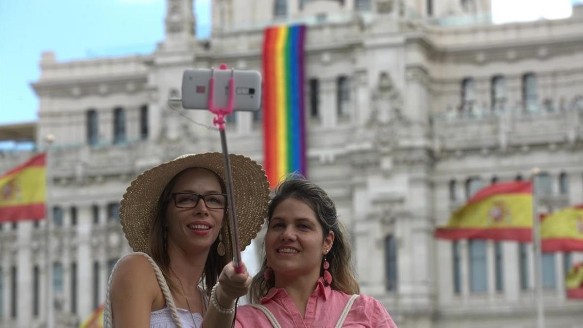 Dos turistas se hacen un 'selfie' frente al Ayuntamiento de Madrid, que luce la bandera del arcoiris.