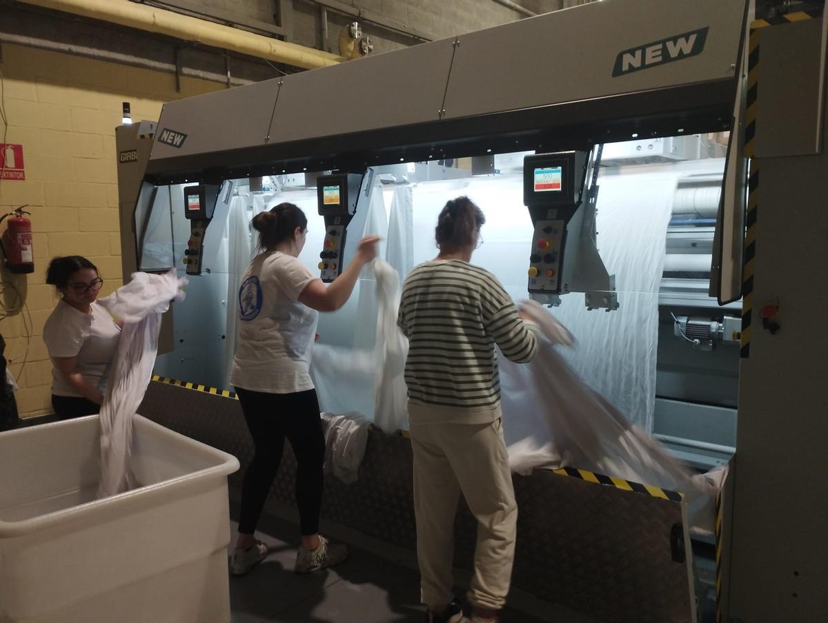 Tres trabajadoras meten sábanas en la máquina para su secado y planchado.