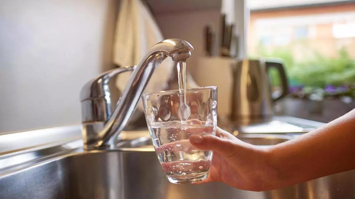 Una persona abre el grifo para llenar un vaso de agua.