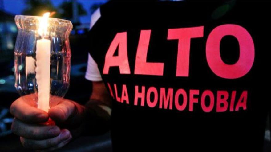 Un activista LGTBI sostiene una vela y reclama el fin de la homofobia en su camiseta.