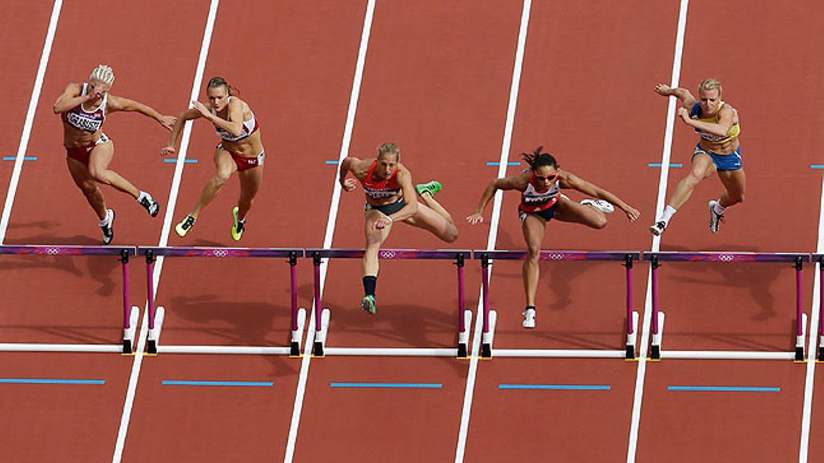 Las atletas femeninas saltan uno de los obstáculos en la carrera de los 100 metros.