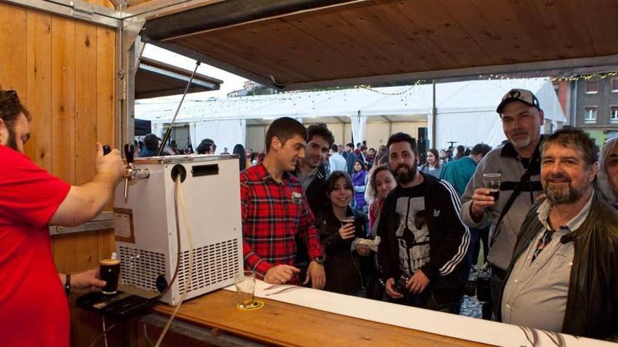 Uno de los expositores tira una cerveza ante varias personas en la carpa de la pinacoteca de Langreo.