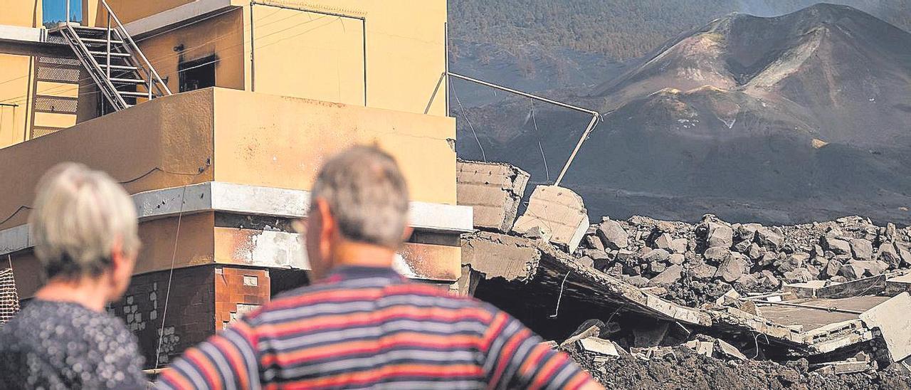 Dos personas observan el volcán Tajogaite y los efectos sobre las viviendas que la lava arrasó a su paso.