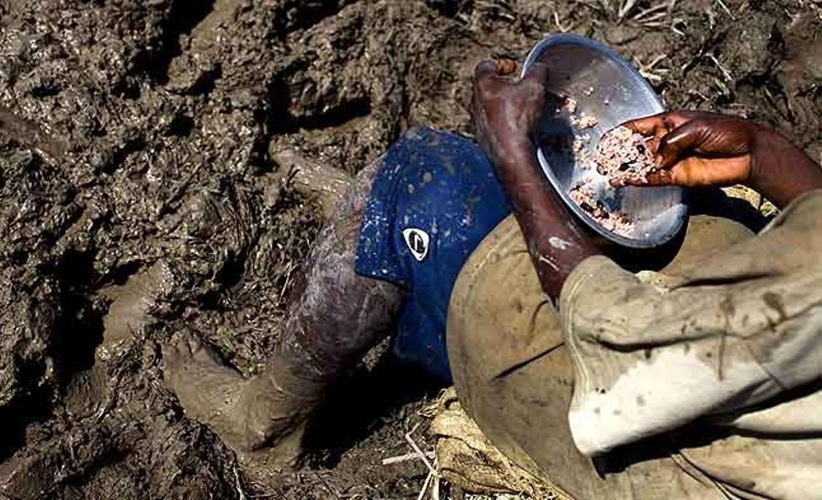 Un cultivador d’arròs menja la seva ració de menjar mentre està assegut en un camp cobert d’aigua fangosa que podria estar contaminada pel bacteri del còlera a Saint-Marc (Haití).