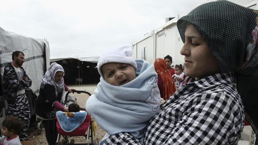 Una madre siria sostiene a su bebé fuera de su tienda de campaña.