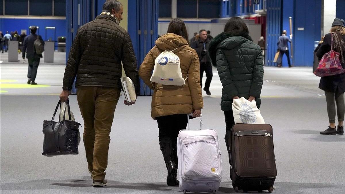 Algunos asistentes a la Cumbre del Clima de Madrid salen del recinto con sus maletas.
