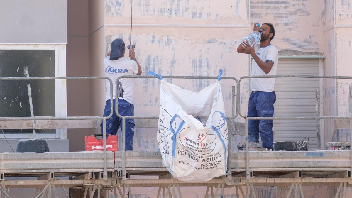 Dos operarios se hidratan mientras trabajan en un andamio en una obra en Alicante