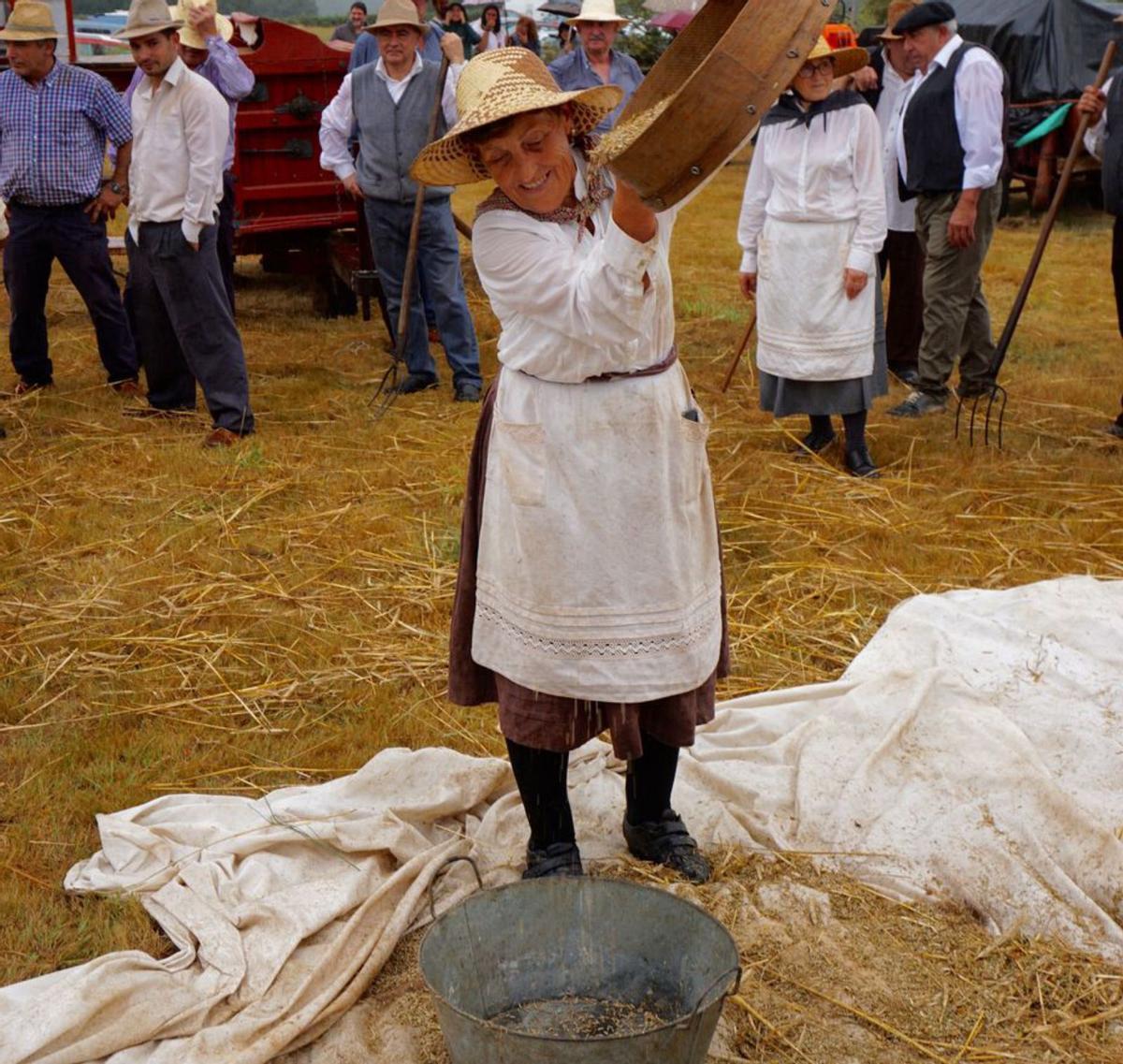 Unu mujer, vestida de época, separa los granos con una criba.